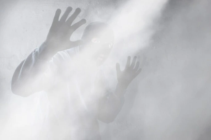 Person mit erhobenen Händen hinter einer dichten Nebelwolke